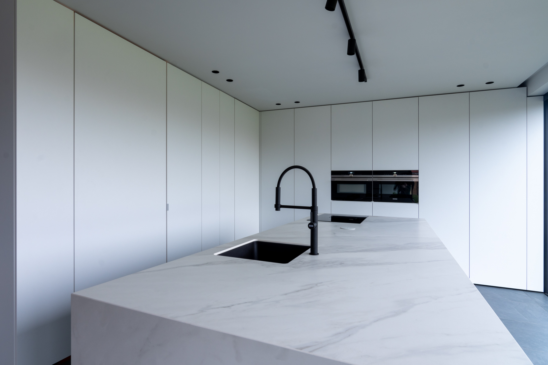 Witte keuken met marmerlook werkblad én zwarte toestellen.
